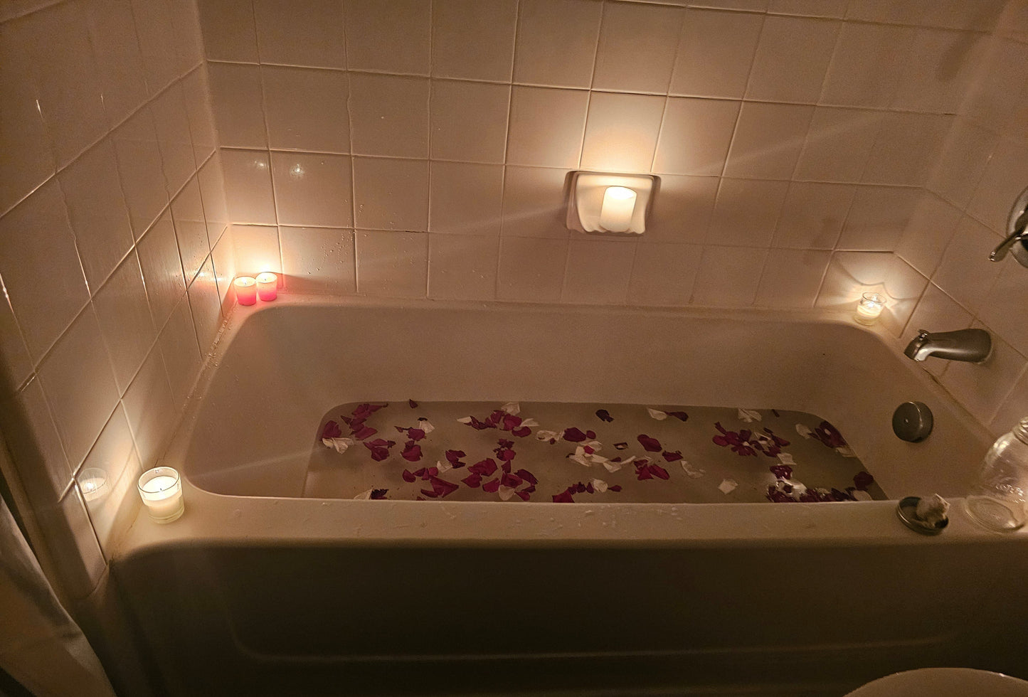 Bath tub with flower petals and candles in a dimly lit bathroom designed by Owls Nest Curios.