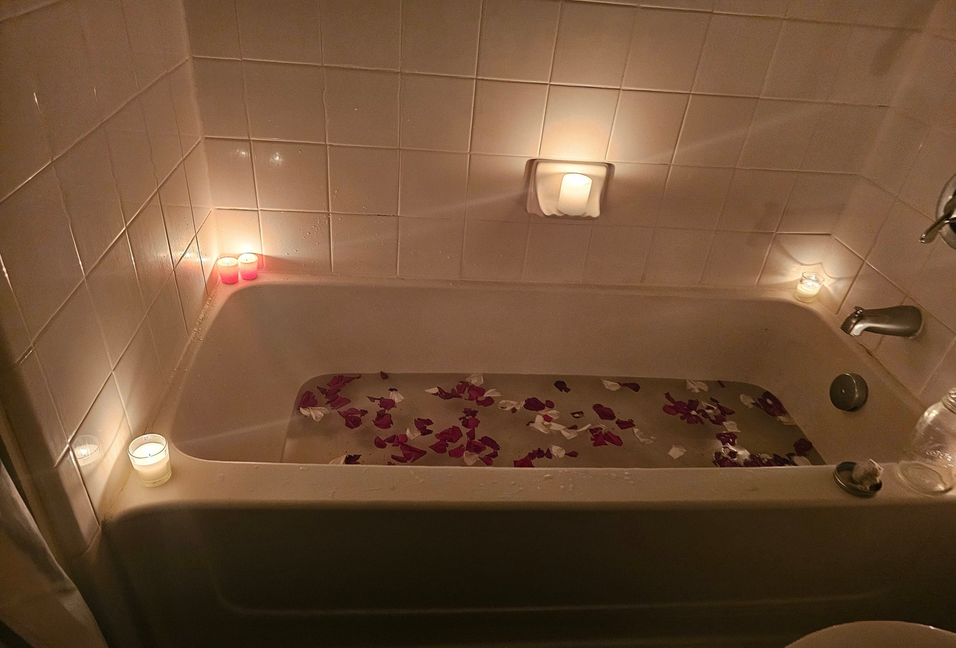 Bath tub with flower petals and candles in a dimly lit bathroom designed by Owls Nest Curios.